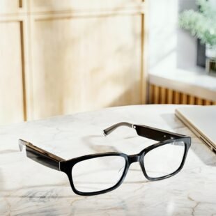 Black glasses on marble desk near laptop.